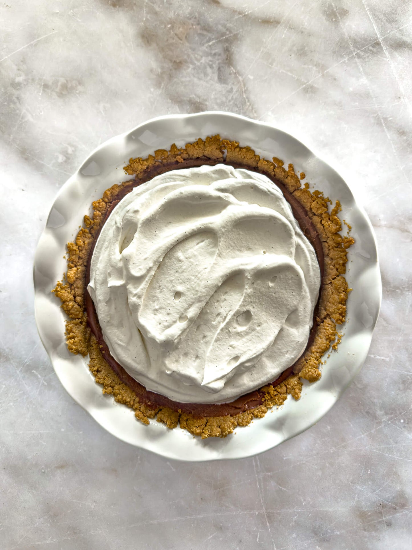 Gluten-free chocolate silk cream pie in a white ruffled-edge pie plate, topped with Madagascan vanilla whipped cream.